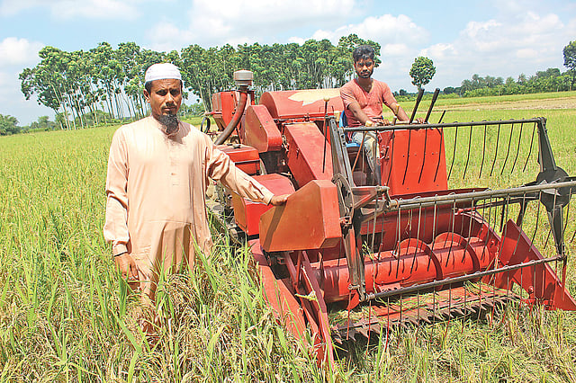 ধান কাটা ও মাড়াইয়ের যন্ত্র কম্বাইন্ড হার্ভেস্টারের পাশে ওলি উল্লাহ (বাঁয়ে)। সম্প্রতি চুয়াডাঙ্গা সদরের শাহাপুরে।  প্রথম আলো