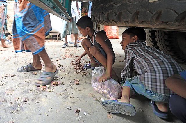 ট্রাকের নিচ থেকে পেঁয়াজ কুড়িয়ে ব্যাগে ভরছে পথশিশুরা। বৃহস্পতিবার বিকেলে তোলা ছবি। ছবি: জুয়েল শীল