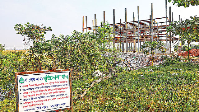 ওয়াসার সাইনবোর্ডে খালের ভেতর অবৈধ স্থাপনা নির্মাণে নিষেধাজ্ঞা দেওয়া হয়েছে। অথচ নিষেধাজ্ঞা ভঙ্গ করা হচ্ছে সাইবোর্ডের পাশেই।