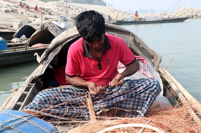 ছিঁড়ে যাওয়া জাল নৌকায় বসে মেরামত করা হচ্ছে।