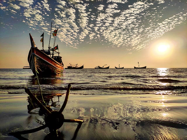 সৈকতে নোঙর করা একটি নৌকা। পাশে ভাসমান আরও কিছু নৌকা।