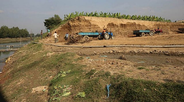 বন্যা নিয়ন্ত্রণ বাঁধের পাশ থেকে কাটা মাটি ট্রাক্টরে করে নিয়ে যাওয়া হচ্ছে। গত বৃহস্পতিবার শিবগঞ্জ মোড় এলাকায়।  ছবি: প্রথম আলো