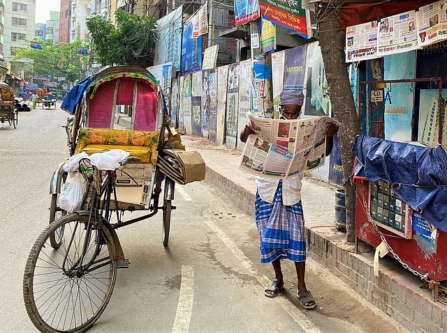 আদাবর ৭ নম্বর সড়কের মসজিদের পাশের একটি সংবাদপত্র বিক্রির দোকানের সামনে পাওয়া গেল লুৎফর রহমানকে। মধ্য দুপুরে রিকশা থামিয়ে দোকানে ঝুলিয়ে রাখা সংবাদপত্র পড়ছিলেন তিনি গভীর মনোযোগ দিয়ে। ছবি: লেখক