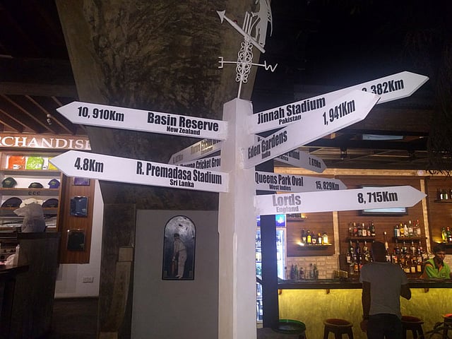 আইকনিক উডেন ট্রাফিক সিগনালে বিশ্বের নামীদামী সব ক্রিকেট ভেন্যুর অবস্থান ও দূরত্ব নির্দেশ করা আছে। ছবি: লেখক