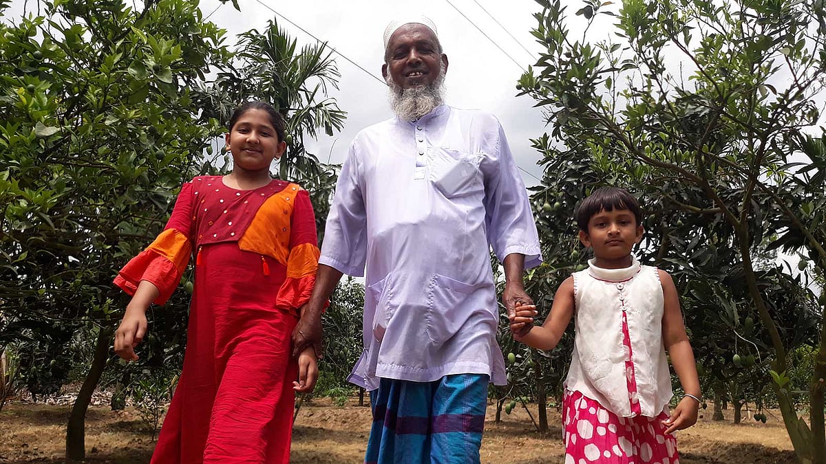 দুই নাতিকে নিয়ে নিজের বাগানে নুরুল ইসলাম মাস্টার। ছবি: লেখক