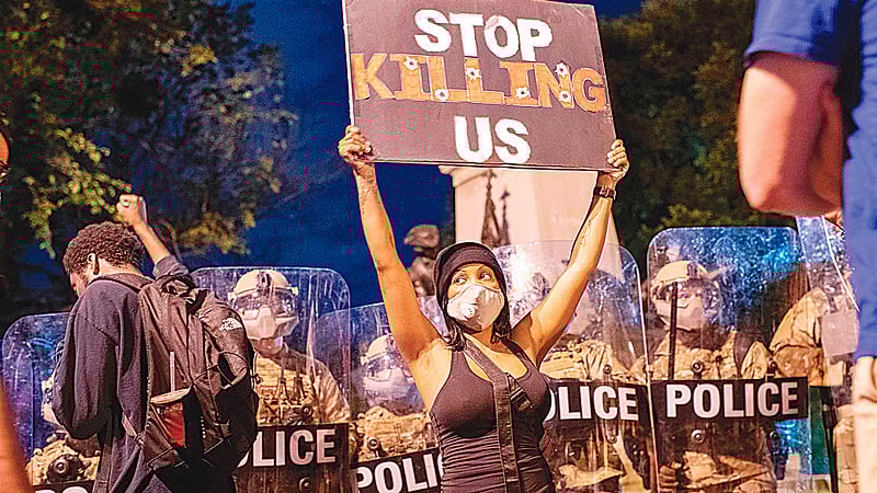 যুক্তরাষ্ট্রের প্রেসিডেন্টের সরকারি বাসভবন হোয়াইট হাউসের সামনে সারিবদ্ধ দাঁড়ানো অস্ত্রসজ্জিত দাঙ্গা পুলিশ। তাঁদের সামনে প্ল্যাকার্ড নিয়ে দাঁড়িয়ে পড়েন এক বিক্ষোভকারী। প্ল্যাকার্ডে লেখা, ‘আমাদের হত্যা বন্ধ করো’। গত শনিবার।  ছবি: এএফপি