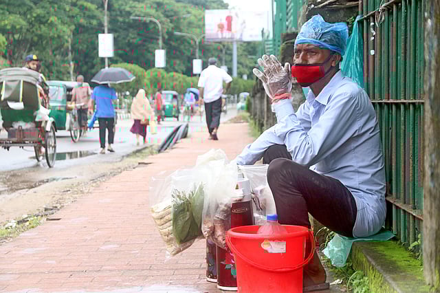 হাতে দস্তানা, মুখে মাস্ক, মাথায় পলিথিন মুড়িয়ে চায়ের ফ্লাক্স নিয়ে ফুটপাতে বসেছেন চা-বিক্রেতা রফিক মিয়া। করোনার কারণে দীর্ঘদিন বন্ধ রাখার পর আবার তিনি ফেরি করে চা বিক্রি শুরু করেছেন। চৌহাট্টা, সিলেট, ১০ জুন। ছবি: আনিস মাহমুদ
