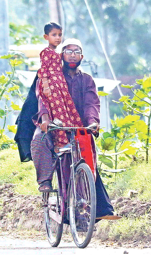 পল্লি অঞ্চলে করোনার সচেতনতা এখনো আসেনি। সাইকেলে বাবার সঙ্গে বাইরে বের হয়েছে এক শিশু। গত শুক্রবার যশোরের শার্শা উপজেলার আমড়াখালী সেতু এলাকায়।  ছবি: এহসান-উদ-দৌলা