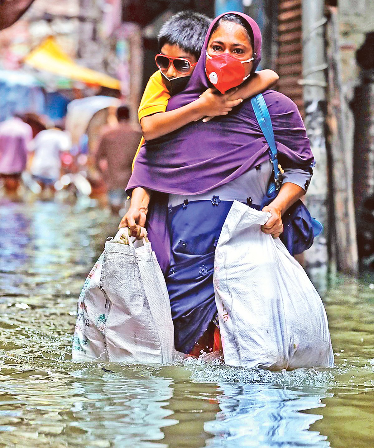 দুই হাতে ভারী ব্যাগ আর ছেলেকে কাঁধে নিয়ে ‘নদী’ পার হচ্ছেন মা জলি আক্তার। এখন একটু বৃষ্টি হলেই ঢাকার রাজপথ যেন নদী হয়ে যায়। গতকাল দুপুরে পুরান ঢাকার আলুবাজার এলাকায়। দীপু মালাকার