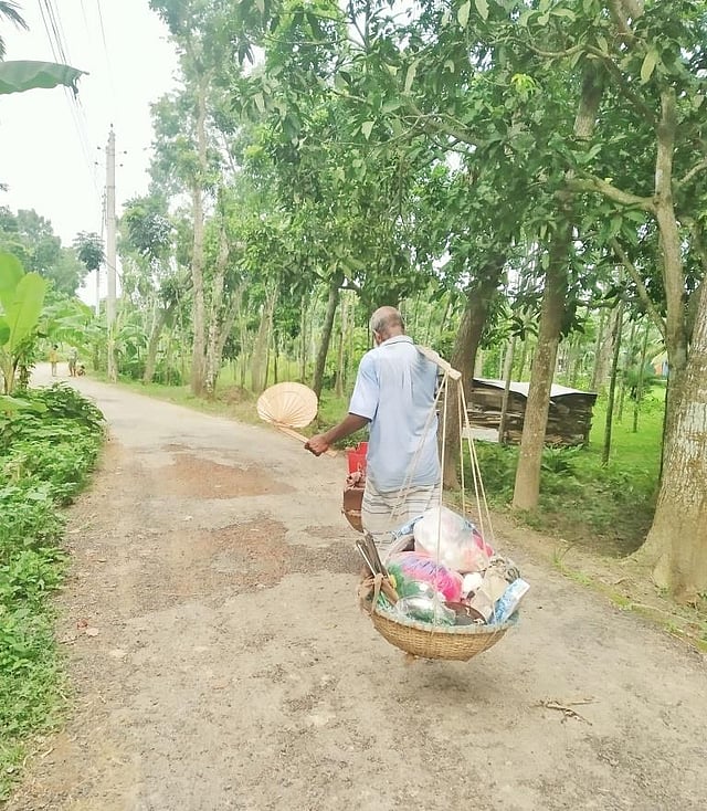প্রচণ্ড গরম, ক্লান্ত দুপুর, করোনাভীতি। তবু ফেরিওয়ালা চলছে জীবিকার অন্বেষণে গ্রাম থেকে গ্রামান্তরে। গরম থেকে বাঁচতেই হাতপাখা নিয়ে ছুটে চলা, তবু পিঠের ঘামে জড়ানো শার্টটা যেন ক্লান্তির প্রতীক। কালুখালী, রাজবাড়ী, ১১ আগস্ট। ছবি: শামিম