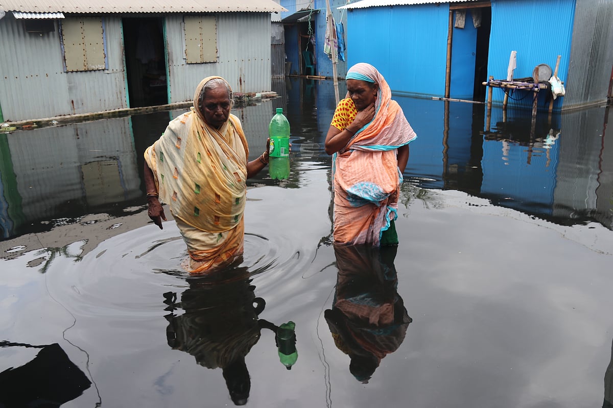 পানিতে তলিয়ে গেছে রহিমা বেগম (ডানে) আর সাহারা বেগমের ঘরসহ টিউবওয়েল। পাশের বাড়িতে যাচ্ছেন পানি সংগ্রহের জন্য।