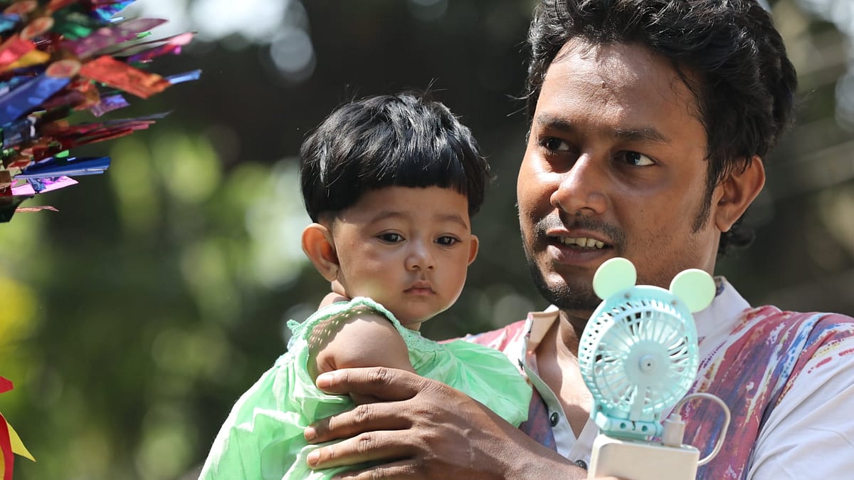 শিশুকে আরাম দিতে ছোট চার্জার ফ্যান হাতে এক অভিভাবক।