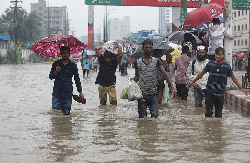 সড়কে হাঁটুসমান পানি। গাড়িও পাওয়া যাচ্ছে না। নিরুপায় হয়ে পানি মাড়িয়ে চলছেন তাঁরা
