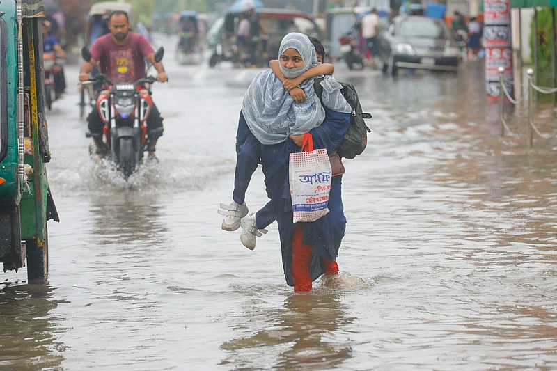 স্কুল থেকে ফেরার পথে শিশুকে পিঠে নিয়ে জলমগ্ন সড়ক পার হচ্ছেন এক মা।