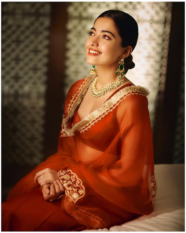 রাশমিকা মান্দানা পোঙ্গাল অনুষ্ঠান উপলক্ষে পরেছেন মরচে লাল লেহেঙ্গা। ওড়নাটি অরগাঞ্জা ফেব্রিকের, রঙ ম্যাচিং। গোটা পাত্তির কাজ আর জরির বর্ডার রয়েছে এতে। 