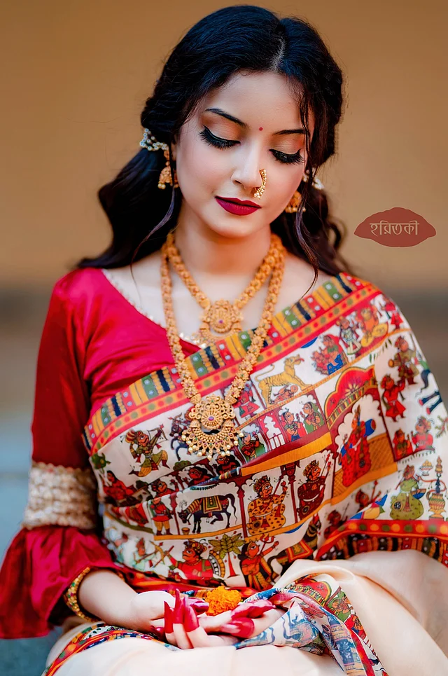 সাদা সিল্কে বহুরঙা ফোক আর্টের ডিজিটাল প্রিন্ট করা শাড়িটি সত্যিই নজরকাড়া। এর সঙ্গে গাঢ় লাল লিপ কালার আর একটু নাটকীয় কিন্তু ট্র্যাডিশনাল সাজ মানাবে। গয়নায় নাকছাবি, দুল আর হারে আনা যায় জমকালো লুক