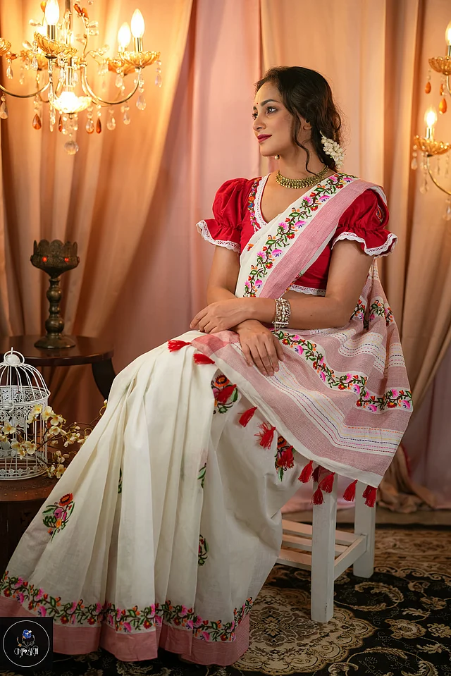 সাদা জমিনে হালকা গোলাপি পাড়। সাদা-লাল সুতার বুননের কারসাজিতেই এমন শেড এসেছে। আঁচলে বহুরঙা স্ট্রাইপ। আর শেহ প্রান্তে লাল ট্যাসেল। 