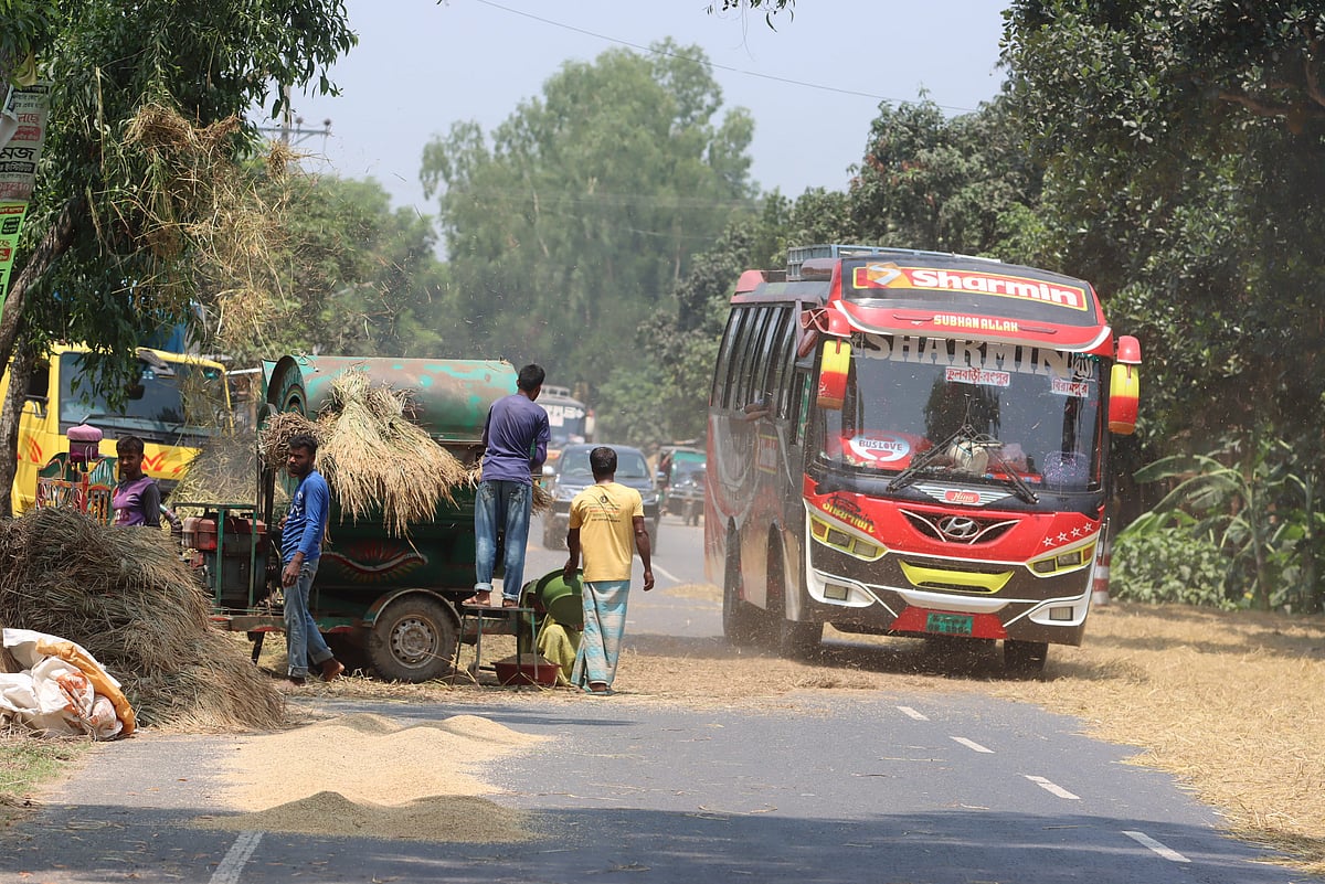 মহাসড়কের এক পাশ দখল করে যন্ত্রে ধান মাড়াই করছেন চাষি। অপর পাশ দিয়ে চলছে দূরপাল্লার যাত্রীবাহী বাস। 