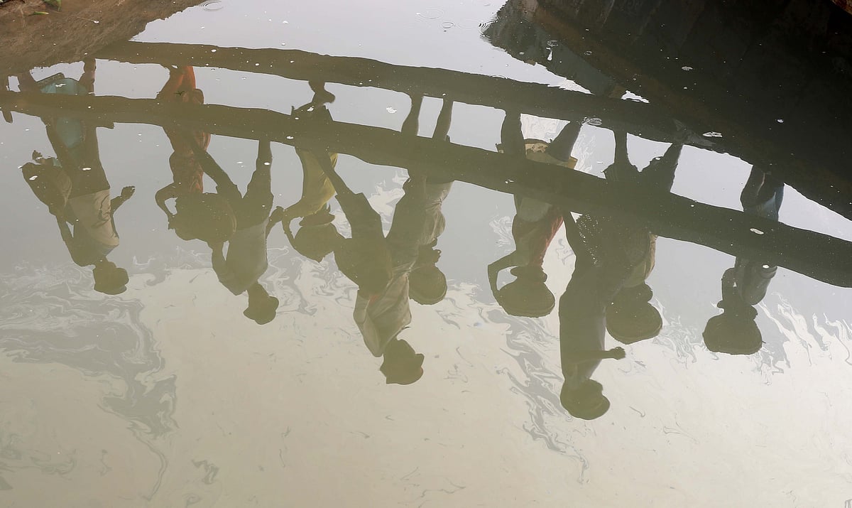 নৌকা থেকে বালু বয়ে নিয়ে যান শ্রমিকেরা। নদীতে তাঁদের প্রতিবিম্ব। 