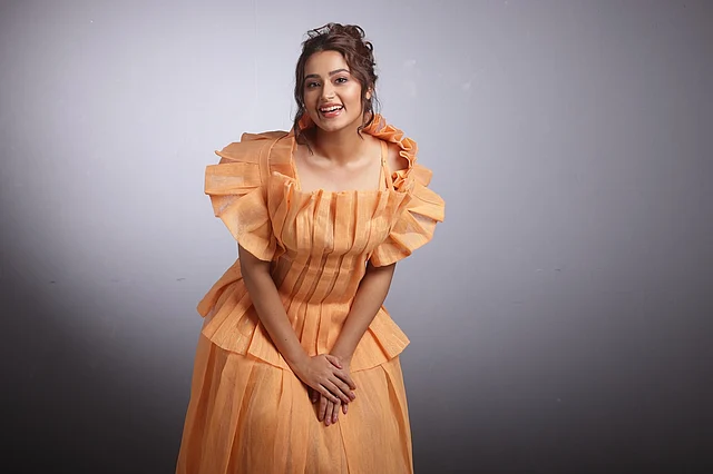 সফট অরেঞ্জ বা হালকা কমলা রঙের স্ট্রাকচার্ড গাউন বলা যেতে পারে এই আউটফিটটিকে। গাউনের ওপরের অংশের পুরোটা জুড়েই আকর্ষণীয় প্লিটেড ডিজাইন। যা অভিনেত্রীর লুকে এনেছে নাটকীয় আমেজ। 