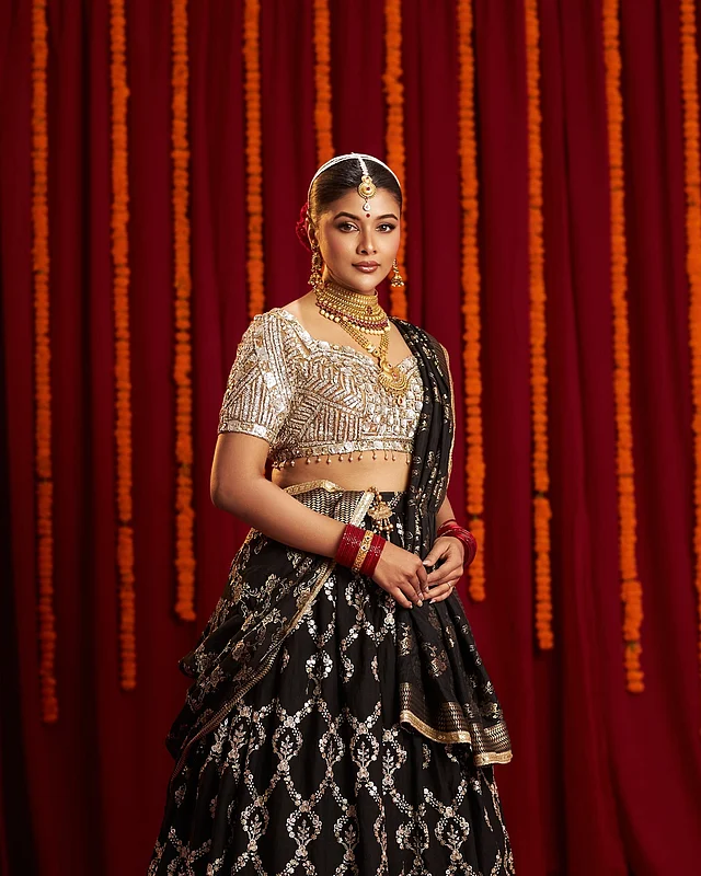 জমকালো লেহেঙ্গার সাজে অভিনেত্রী মুমতাহিনা চৌধুরী টয়া। নানা কাটের গোল্ডেন সিকুইনের সুইটহার্ট নেকলাইন ব্লাউজের সঙ্গে বিশেষভাবে নজর কাড়ছে বটমের অংশটুকুও। বটমের কালো জমিনে গোল্ডেন এমব্রয়ডারি করা ফ্লোরাল কারুকাজ। সঙ্গে আছে ম্যাচিং ওড়না। গোল্ড প্লেটেড ভারী গয়না, খোঁপায় দেওয়া লাল গোলাপ আর সফট গ্ল্যাম মেকআপ লুকে এনেছে আভিজাত্য।
