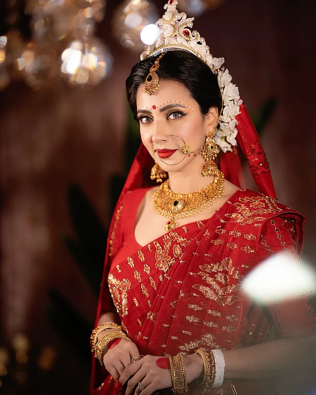 লাল টুকটুকে সনাতনী ব্রাইডাল লুকে ক্যামেরায় ধরা দিয়েছেন অভিনেত্রী বিদ্যা সিনহা মিম। পরেছেন সোনালি জরি সুতার কাজের লাল জামদানি। সঙ্গে কনুইহাতা ম্যাচিং ব্লাউজ। আকর্ষণীয় সোনার গয়নায় সেজেছেন। হাতে শোভা পাচ্ছে আলতা আর শাঁখা-পলা। মাথায় জামদানি ওড়না ছাড়া পরেছেন খুব সুন্দর একটা শোলার মুকুটও। লাল টিপ, কপাল চন্দন, লাল লিপস্টিক, সোনালি আইশ্যাডো আর আইলাইনারে তাঁকে লাগছে অপূর্ব।