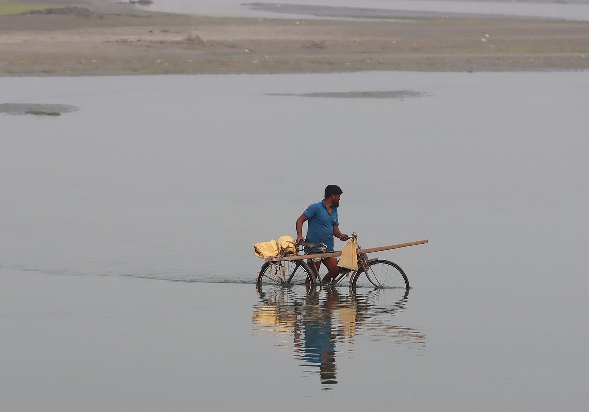 সাইকেল নিয়ে নদী পার হচ্ছেন একজন কৃষক। 