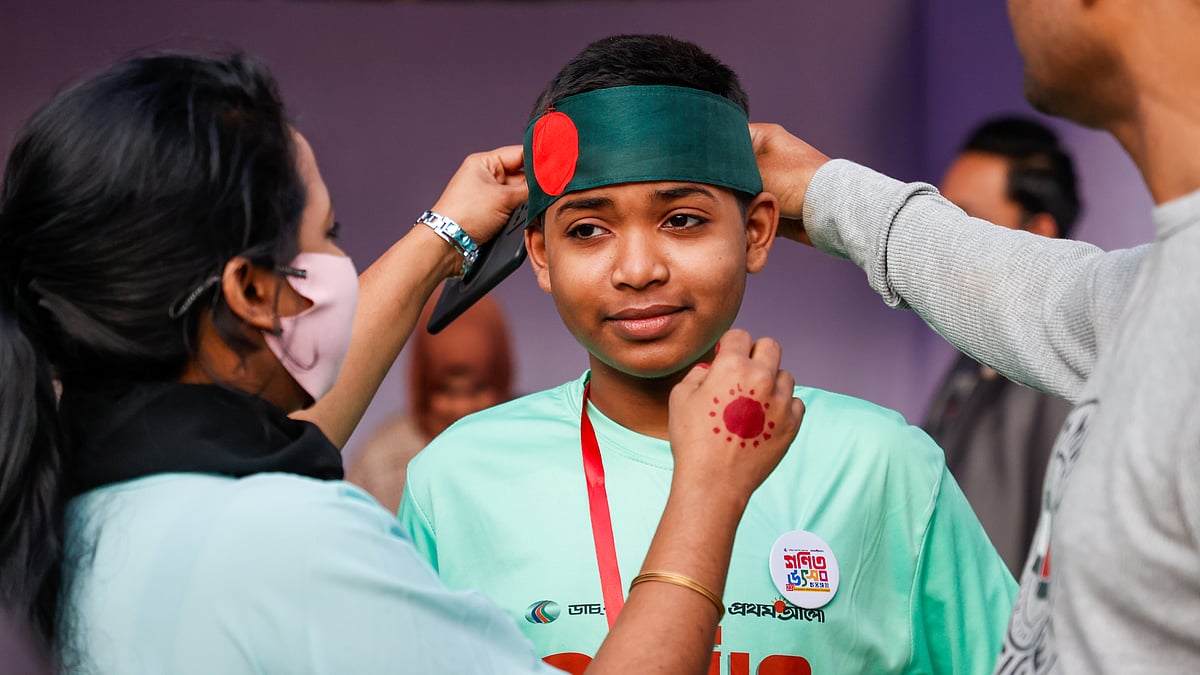 জাতীয় গণিত উৎসব ২০২৫–এ অংশ নেওয়া এক শিক্ষার্থীর মাথায় জাতীয় পতাকা বেঁধে দিচ্ছেন অভিভাবক।