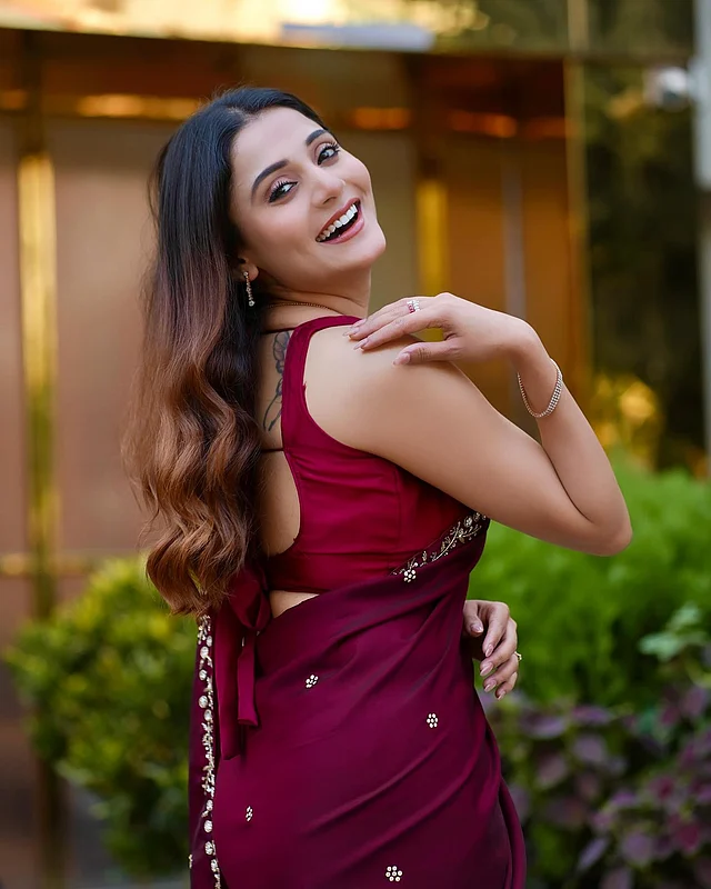 জাম রঙের শাড়ির সঙ্গে ব্যাকলেস ব্লাউজ জুটি হয়েছে এই লুকে। হানি ব্লন্ড কালার চুলগুলো ছেড়ে রাখা হয়েছে সফট কার্ল স্টাইলে