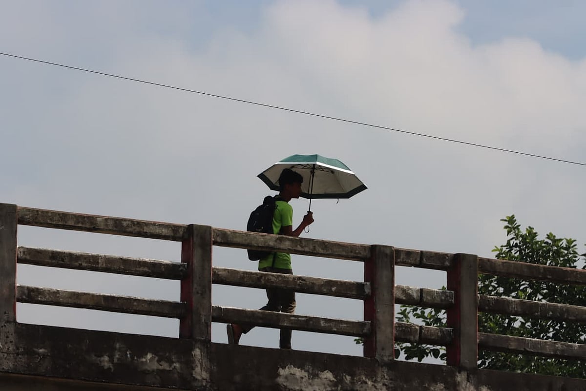 রোদের মধ্যে ছাতা মাথায় বিদ্যালয়ে যাচ্ছে এক শিক্ষার্থী। 
