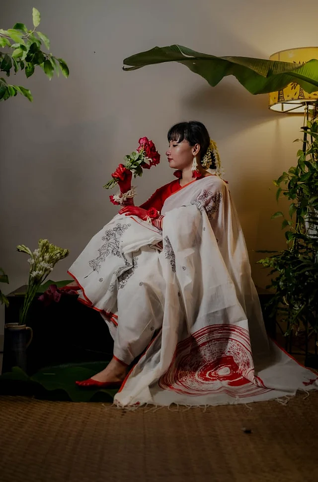 চিকন লাল পেড়ে সাদা ক্ল্যাসিক শাড়িটি করা হয়েছে শিউলি গাছের মোটিফে। কালো রঙে করা হয়েছে এই নকশা। আঁচলে অ্যাবস্ট্রাক্ট নকশাটি করা হয়েছে লাল রঙে ।