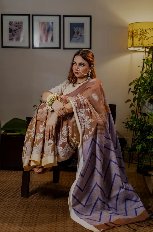 ভিন্টেজ আমেজে করা হয়েছে মাটির মতো হালকা বাদামি-বেইজ ডুয়েল টোনের এই শাড়িটি । এই শাড়ির নকশা হিসেবে দেখা যাচ্ছে ট্রাইবাল মোটিফ। আঁচলে নীল জিগজ্যাগ জ্যামিতিক রেখা আধুনিক একটা বৈপরীত্য তৈরি করেছে এই শাড়িতে। 