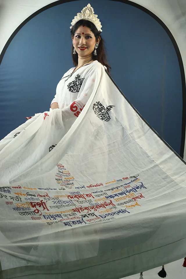 দেবীদুর্গার ১০৮টি নাম দিয়ে এই শাড়িটি করা। প্রদীপ আকারে নামগুলো উঠে এসেছে। জমিনে ছোট আর আঁচলে বড় প্রদীপের আদলে নামগুলোর নান্দনিক বিন্যাসে স্ক্রিন প্রিন্টে ফুটিয়ে তোলা হয়েছে। আঁচলে আরও ব্যবহার করা হয়েছে লাল, সাদা ও কালো ট্যাসেল। 