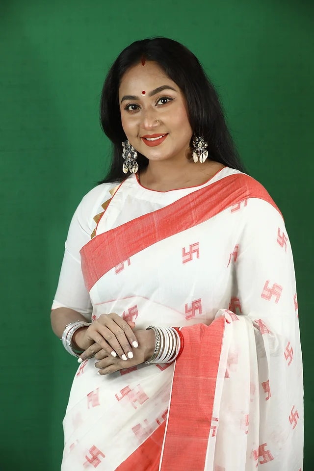 পূজায় লালপেড়ে সাদা শাড়ি সাধারণত থাকে চাহিদার শীর্ষে। তার ওপর এমন থিমেটিক হলে তো কথাই নেই। সাদা জমিনে লাল সুতার বুননে ফুটিয়ে তোলা হয়েছে স্বস্তিকা চিহ্ন। আঁচলে স্ক্রিন প্রিন্টে অলংকৃত ত্রিনয়নী মোটিফে সোনালি নোলকের ডিটেইলও নজর কাড়ে।