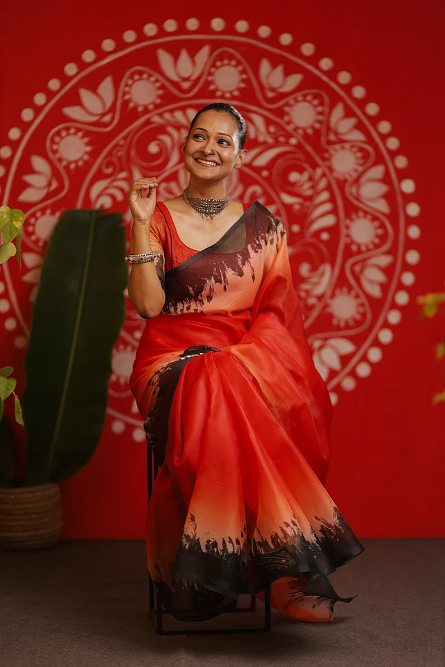 উৎসবে লাল রং যেন সব সময়ই বিশেষ গুরুত্ব পায়। হালকা কমলা আভার এই লাল শাড়িও ব্যতিক্রম নয়। শাড়ির কালো পাড়ে ডিজিটাল প্রিন্টের মাধ্যমে ফুটিয়ে তোলা হয়েছে শরতের কাশফুল। 