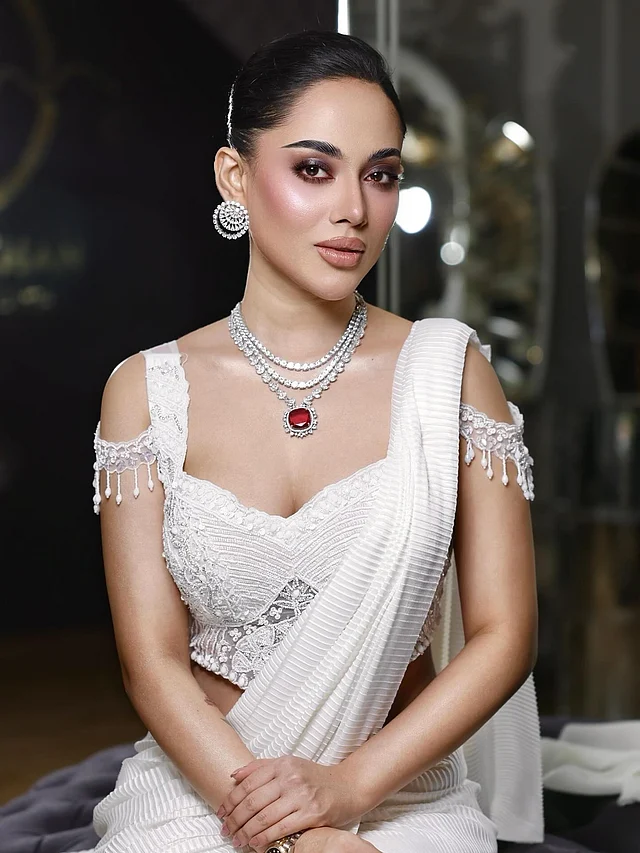 এখানে নজরকাড়া এমবেলিশমেন্টের সাদা ডিপ সুইটহার্ট নেকলাইনের স্লিভলেস ব্লাউজ আর সাদা ক্রেপ ফেব্রিকের শাড়িতে দেখা যাচ্ছে তাঁকে