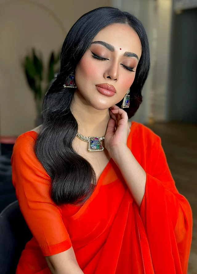 মেকওভারটি এ লুকের হাইলাইট। কপার টোনের আই শ্যাডো, ফুল লিপসের সেমি গ্লসি ফিনিশ, টেনে দেওয়া আইলাইনার, ছোট লাল টিপ, পরিমিত ব্লাশ অনের ব্যবহারে চোখজুড়ানো সফট গ্ল্যাম লুকের সঙ্গে সোনায় সোহাগা হয়েছে ওয়েভি হেয়ারস্টাইল