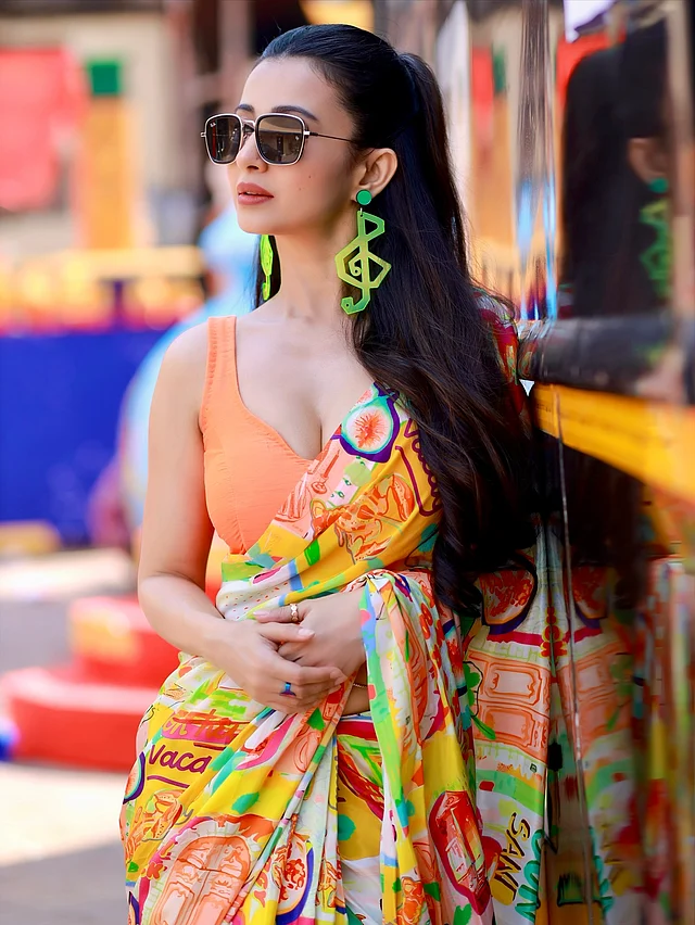 ফ্যাশনে বরাবরই এক ধাপ এগিয়ে কলকাতার অভিনেত্রী মনামী ঘোষ। এই লুকে তিনি পরেছেন পপ-আর্ট প্রিন্টের সিল্ক শাড়ি। শাড়ির বেজ রং সাদা হলেও এর ওপর ছড়িয়ে আছে উজ্জ্বল কমলা, হলুদ, সবুজ ও লালের নকশা—যেন ক্যানভাসে রঙের উৎসব! এর সঙ্গে জুটি হওয়া কমলা ব্লাউজের ডিপ নেকলাইন ও স্লিভলেস কাট পুরো লুকটিকে দিয়েছে আধুনিক আবেদন। 