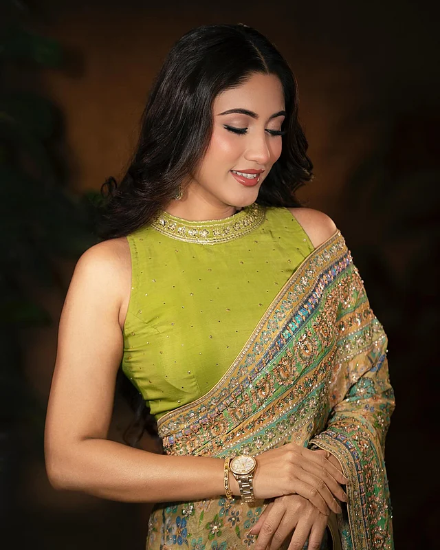 শাড়ির সঙ্গে মানানসই লাইম অলিভ রঙের ব্লাউজটি স্লিভলেস ও হাই-নেক ডিজাইনের। সোনালি জড়িসুতা আর সিকুইনের নেকলাইনটিও আকর্ষণ কাড়ছে।