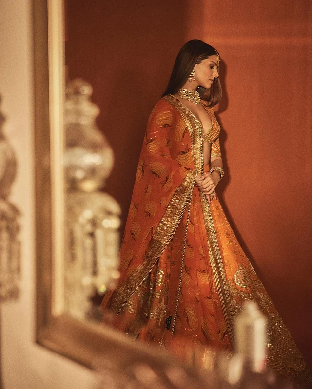 তারা সুতারিয়ার কমলা রঙের লেহেঙ্গাটি যেন একেবারে ব্রাইডসমেইডদের স্বপ্নের পোশাক। সূক্ষ্ম এমব্রয়ডারি, নরম ফ্লোই কাট, আর ভারী চাকচিক্যের মাঝেও রয়েছে এক ধরনের মিনিমালিজম