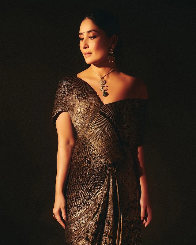 বিখ্যাত ভারতীয় ডিজাইনার অমিত আগরওয়ালের পোশাকে  কারিনা। কালো ও সোনালি প্রি-ড্রেপড ভিনটেজ বেনারসির রাজকীয় আমেজ ধরা পড়েছে তাঁর লুকে। পুরো শাড়ির জমিনে কালো সুতা আর সোনালি জরির দৃষ্টিনন্দন কাজ মুগ্ধ করবেই। এই শাড়িকে প্লিটে নান্দনিকতায় দারুণ দক্ষতার সঙ্গে ফুটিয়ে তোলা হয়েছে গাউনের আমেজ। প্লিট করা ড্রেপিংয়ে মুনশিয়ানার সঙ্গে অফ শোল্ডার নেকলাইন দিয়েছে বিশেষ মাত্রা। 