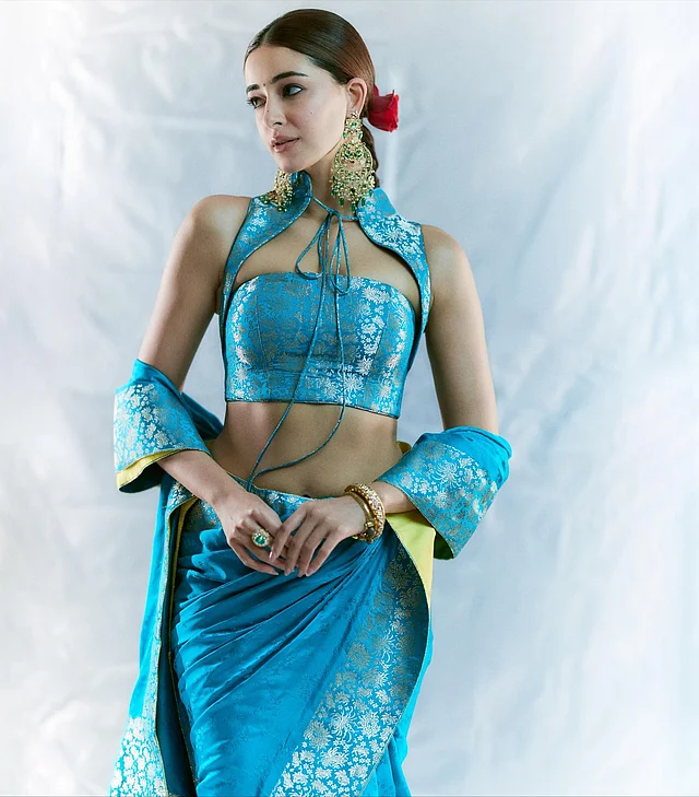 অনন্যা পান্ডে সব সময়ই ফ্যাশনের ফেবারিট। সম্প্রতি তিনি বেনারসির শাড়ি-গাউনের মাধ্যমে ঐতিহ্যকে নতুনভাবে উপস্থাপন করেছেন। লুকের কেন্দ্রবিন্দু হলো স্টানিং টারকোয়াইজ-নীল বেনারসি শাড়ি। ফেব্রিকে রয়েছে রাজকীয় জারি মোটিফের সঙ্গে গোল্ডেন ফ্লোরাল প্যাটার্ন। তবে সত্যিই এই লুককে আলাদা করেছে ড্রেপিং স্টাইল বা শাড়ি পরার ধরন। 