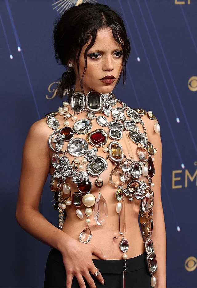  এ বছর এমি অ্যাওয়ার্ডসের সবচেয়ে বোল্ড লুক বলা যায় জেনা ওর্টেগার জিভাঁশির পোশাককে। এদিন চোখ কপালে তোলা রেড কার্পেট লুকে দেখা যায় তাঁকে। ‘ওয়েনসডে’-এর চরিত্র যেন পেয়ে বসেছে হলিউডের জেন–জি সেনসেশনকে নিজের গথিক ডার্ক লুক ধরে রেখে পরেছেন বডি জুয়েলারি স্টাইল ব্রালেট-টপ। পাথর ছাড়া আর কোনো কিছুই নেই এতে