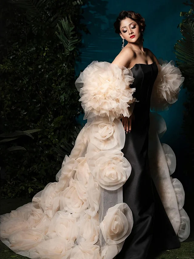 পূজা চেরির পরনে স্ট্র্যাপলেস ব্ল্যাক কোরসেট গাউ । লুকের আসল আকর্ষণ গাউনের সঙ্গে জড়ানো ক্রিম শেডের বিশাল ফুলেল ট্রেন। যেন হাতে গড়া অসংখ্য বড় গোলাপ গায়ে জড়িয়ে নিয়েছেন তিনি। অর্গাঞ্জা ফেব্রিকের থ্রি-ডি ফুলগুলো গাউনটিকে দিয়েছে এক চমৎকার ড্রামাটিক আমেজ 