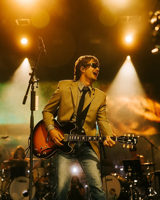 ডিআইওয়াই (DIY) ম্যাগাজিনের এপ্রিল ২০২৫ সংখ্যার প্রচ্ছদে জো কেরিকে দেখা যাচ্ছে গাঢ় ব্লেজার বা জ্যাকেট, হালকা শার্ট এবং গাঢ় নীল ডেনিম জিনসে স্টাইলিশ ক্যাজুয়াল লুকে। পায়ে কালো চামড়ার শু, কালো সানগ্লাস এবং পকেটে হাত রাখা ভঙ্গি লুকটিকে আরও আকর্ষণীয় করেছে।