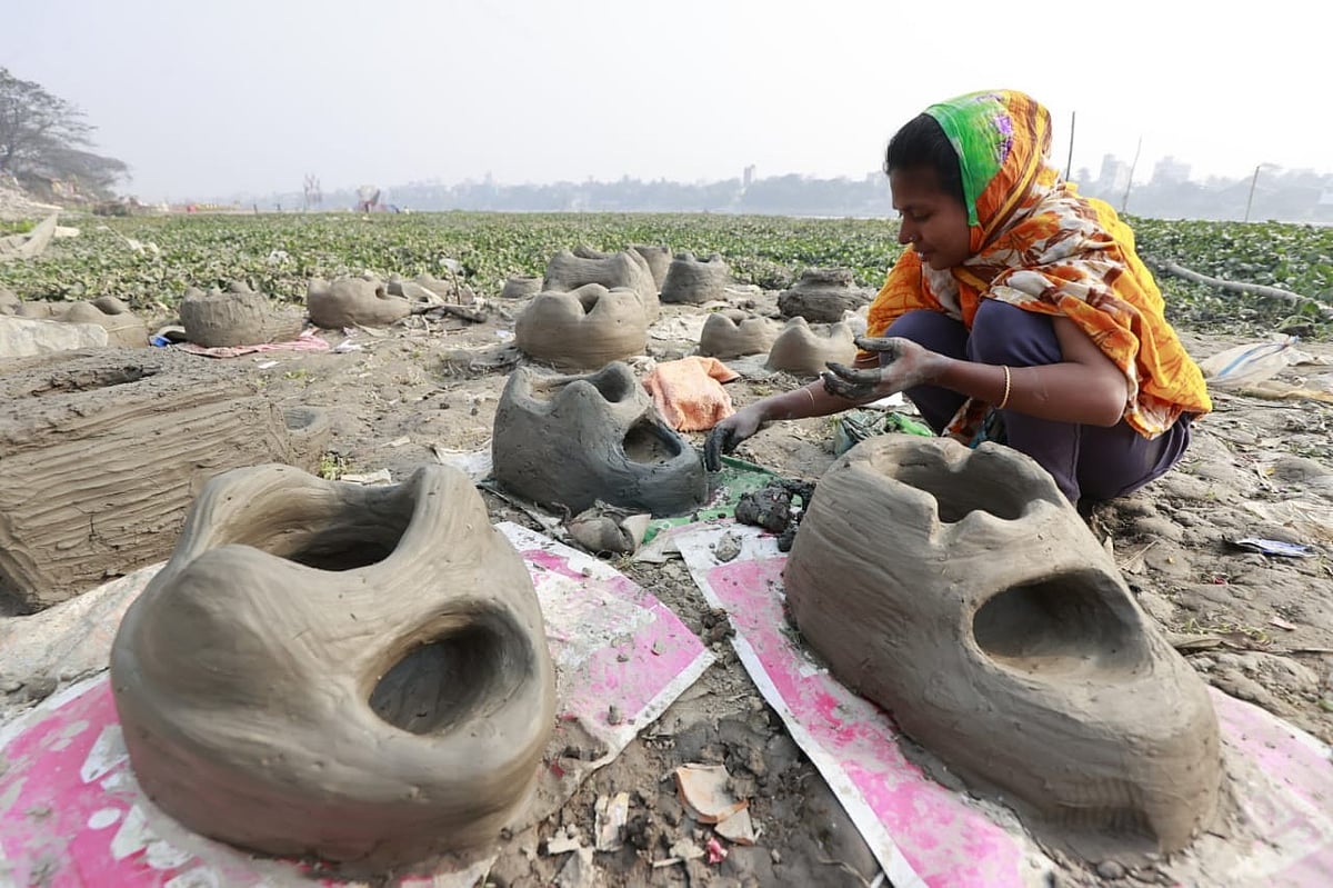  কামরাঙ্গীরচরে বুড়িগঙ্গা নদীর ধারে বসে মাটির চুলা বানাতে ব্যস্ত এক নারী।