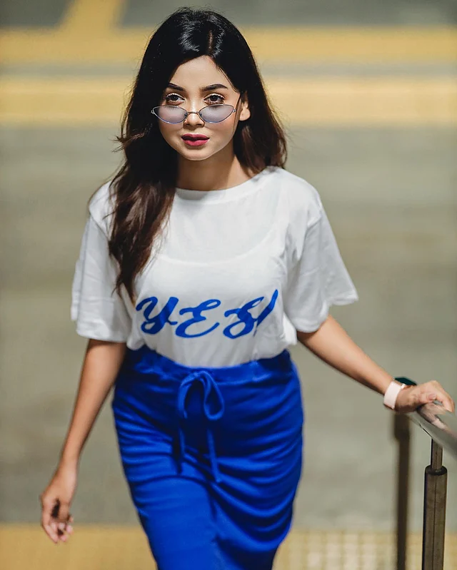 এখানে রঙিন শেডস, সাদা টপ ও নীল স্কার্ট পরেছেন তিনি