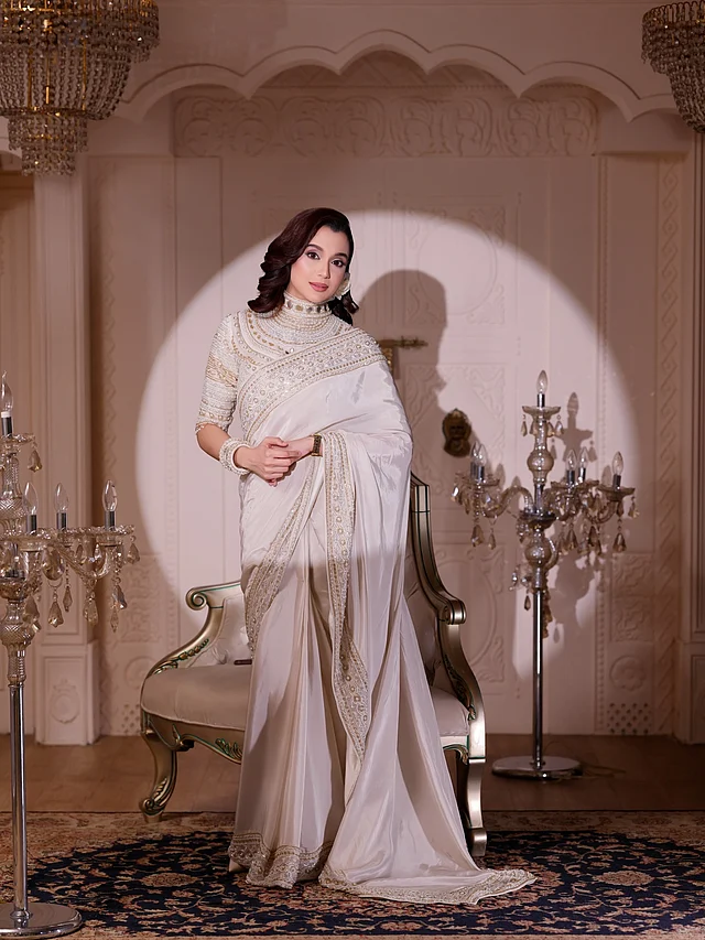 হালকা আইভরি রঙের এই চোখজুড়ানো শাড়িটিতে রয়েছে সূক্ষ্ম সোনালি এমব্রয়ডারি ও মুক্তা-বিডসের কাজ করা বর্ডার। শাড়ির আঁচল জুড়েও রয়েছে একই ধরনের কারুকাজ, যা পুরো লুকটিকে দিয়েছে পরিপাটি আবেদন। 