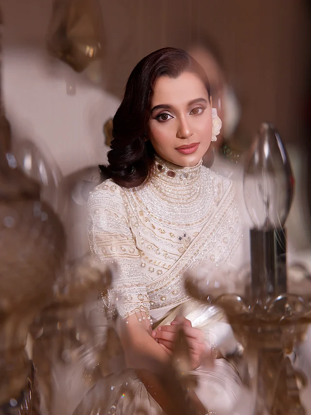 শাড়ির সঙ্গে তিনি পরেছেন হাই-নেক ডিজাইনের ভারী এমব্রয়ডারির ব্লাউজ, যা আলাদাভাবেই নজর কাড়ে। 
ব্লাউজজুড়ে রয়েছে মুক্তা, বিডস ও মিরর ওয়ার্কের চোখধাঁধানো সূচিকর্ম। গলার কাছে কলারধাঁচের নকশাটিই এর মূল আকর্ষণ, যা আলাদা করে ভারী গয়নার প্রয়োজন যেন কমিয়ে দিয়েছে। ফলে পুরো লুকেই তৈরি হয়েছে সংযত অথচ রাজসিক এক ভারসাম্য। 