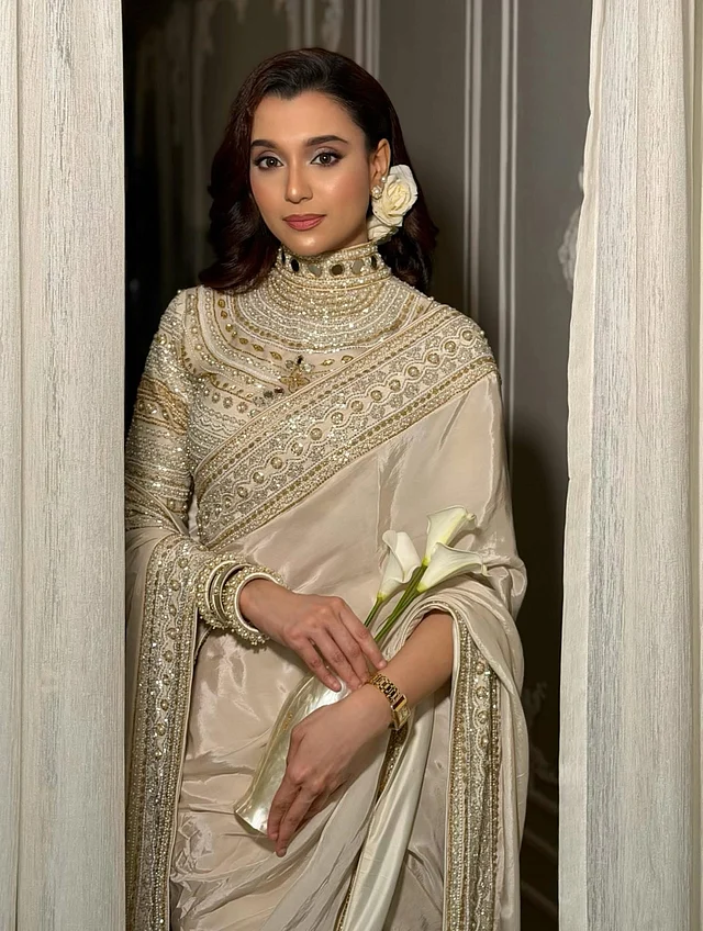 চুল সাইড পার্ট করে নরম ঢেউ খেলানো স্টাইলে রাখা হয়েছে। পাশে গোঁজা সাদা গোলাপ পুরো লুকটিতে যোগ করেছে কোমল আবেদন।